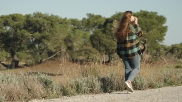 森の背景に向かって道を歩いている若い女性は 彼女の長い髪をまっすぐにします サイドビュー — ストック動画