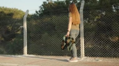 Genç bir kadın çitlerle çevrili bir ormanın yakınında yürüyor. Ağdan ve dikenli tellerden yapılmış, güneşli ve açık hava. Yavaş çekim