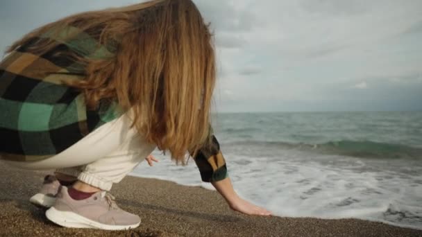 一个蹲在海边的年轻女子碰了碰海浪 后退了 慢动作 — 图库视频影像
