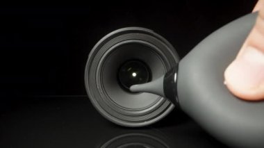 Siyah bir arkaplandaki dijital kameranın lensini, Kauçuk Ampul Hava Pompası Temizleyicisi ile tozunu üflerim.