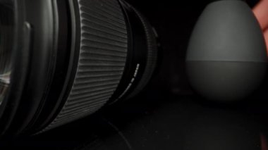 Kameranın lensi siyah cam bir masanın üzerinde. Plastik hava pompasıyla tozunu alıyorum.