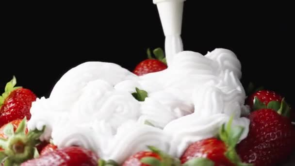 Schlagsahne Wird Aus Einem Spritzbeutel Auf Rotierende Erdbeeren Auf Schwarzem — Stockvideo
