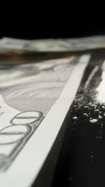 バーティカルビデオ 100ドル紙幣は黒いテーブルに散らばっており 白い粉末は紙幣からチューブに吸い込まれている ドリースライダー極端なクローズアップ — ストック動画