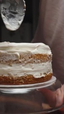 Bayan pasta şefi kremayı pasta için sünger pasta tabakalarına katmanlar halinde yayıyor. Dikey video.