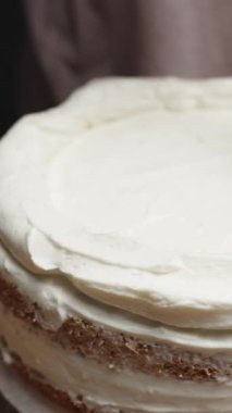 Genç bir kadın pastanın üstüne beyaz krema sürüyor. Dikey video.