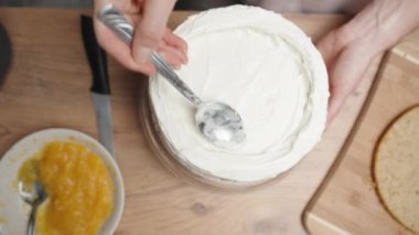 Yukarıdan, bir pasta şefi beyaz kremayı ahşap bir masanın üstüne sürüyor..