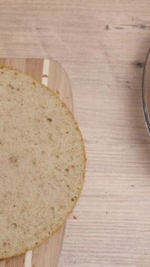 Yukarıdan, ahşap bir masanın üzerinde turuncu komposto dolgulu ve kremalı bir pasta için malzemeler hazır. Dikey video.