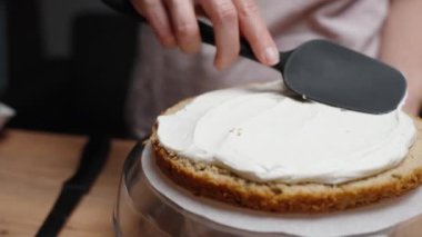 Pasta şefi pandispanya katmanına beyaz krema sürüyor..