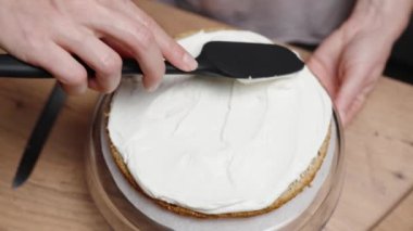 Yukarıdan, bir pasta şefi pasta tabakasına beyaz krema sürüyor..