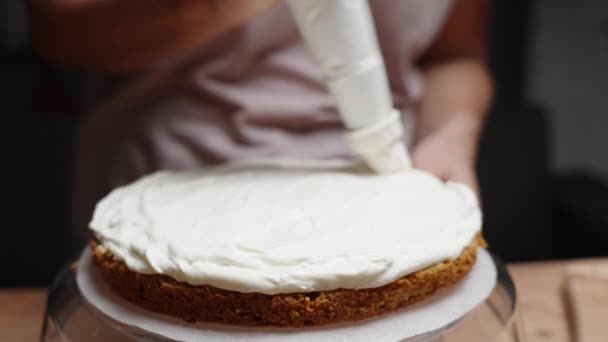スローモーションでは クローズアップショットで 女性はケーキの層の端に沿って白いクリームを適用するペストリーバッグを使用しています — ストック動画