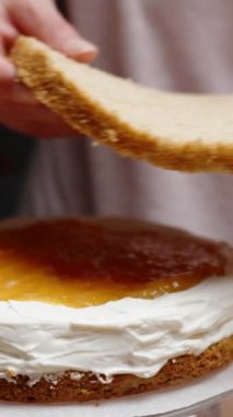 Pasta şefi pastayı birleştirir, turuncu komposto dolgusunun üzerine yavaş çekimde bir katman sünger kek koyar. Dikey video.