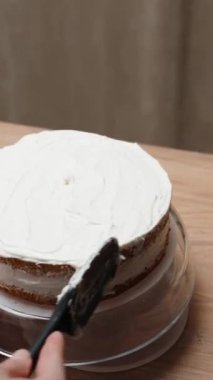 Pastanın üzerindeki kremayı yavaş çekimde düzleştiren kadının arkasından bakın..