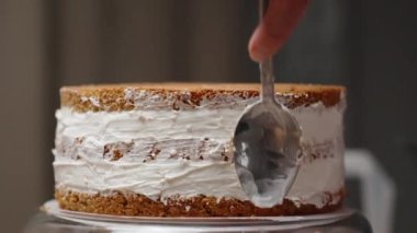 Pasta şefi kremayı sünger kekinin kenarına kadar yumuşatmak için kaşık kullanıyor..