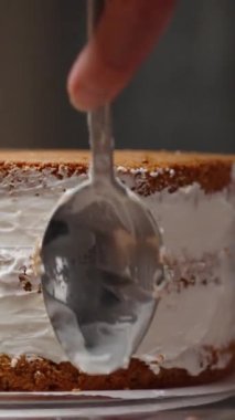 Pasta şefi kremayı sünger kekinin kenarına kadar yumuşatmak için bir kaşık kullanıyor. Dikey video.