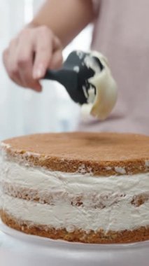 Bir kadın bisküvi keklerinin üzerine krema sürüyor ve pasta yapıyor. Dikey video.