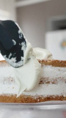 Kadın bir spatula kullanarak pastanın kenarlarına beyaz krema sürüyor. Dikey video.
