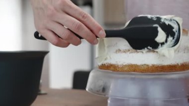 Bir kadın siyah spatula kullanarak bisküvi katmanlarına beyaz krema sürüyor. Pasta hazırlama.