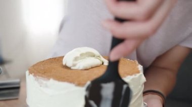 Bir pasta şefi sünger kekinin kenarlarına beyaz krema sürer..