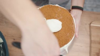 Süngerli kekin kenarlarına krema döken bir kadının tepeden aşağı görüntüsü..