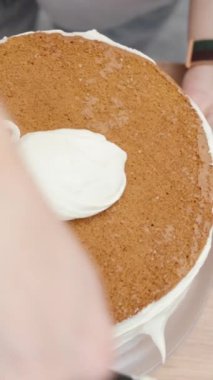 Sünger kekin kenarlarına krem sürmüş bir kadının yukarıdan aşağı görüntüsü. Dikey video.