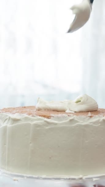 女性はケーキにホワイトクリームを入れ ゆっくりと黒いスパチュラで広げています バーティカルビデオ — ストック動画