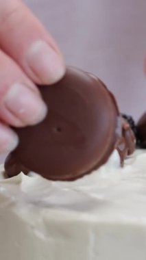 Pasta şefi süs olarak beyaz pastanın üstüne yuvarlak bir çikolatalı kurabiye koyar. Dikey video.