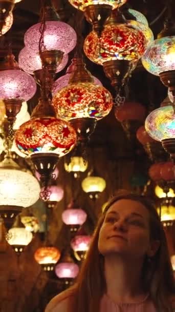 一位年轻女子正在检查挂在一家商店天花板上的色彩艳丽的土耳其古灯 垂直录像 — 图库视频影像