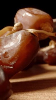 Kamera masanın içinde süzülürken, daldan kurumuş tarihleri topluyorum, süper makro bir çekimle. Dikey video.