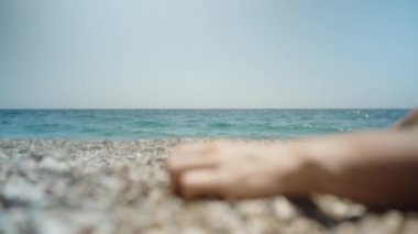 Kamera dikkati denizden bir kadının eline kayalık sahile çakıl taşları dökerken, yakın plan çekimde çeker..