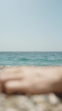 Kamera dikkati denizden bir kadının eline kayalık sahile çakıl taşları dökerken, yakın plan çekimde çeker. Dikey video.