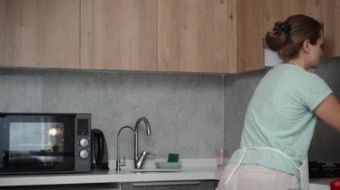 Parlak bir mutfağın panoramik manzarası. Önlük giymiş, nektarin temizleyen genç bir kadın..