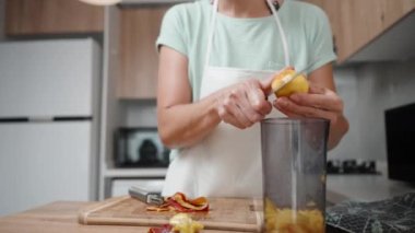 Beyaz önlüklü bir kadın, mikser kullanarak karıştırmak için bir bardakta nektarları küçük parçalara ayırıyor..