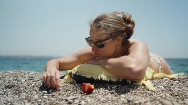 Mayolu genç bir kadın kumsalda güneşleniyor ve çakıl taşlarını istifliyor..