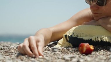 Genç bir kadın deniz kenarında güneşleniyor ve yakın plan çekimde çakıl taşlarını istifliyor..