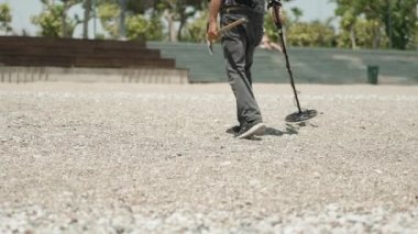 Güneşli bir günde, adamın biri elinde metal dedektör ve kazmayla sahilde yürür..