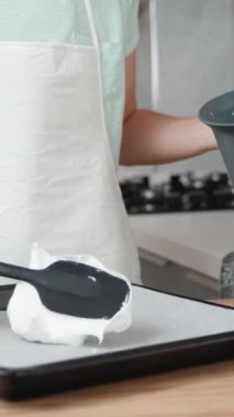 Beyaz önlüklü kadın, parşömen kağıdıyla kaplı bir fırın çarşafına krema sıkıyor. Dikey video.