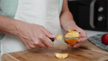 Beyaz önlüklü bir kadın, ahşap bir kesme tahtasıyla nektarini yavaş çekimde kesiyor..