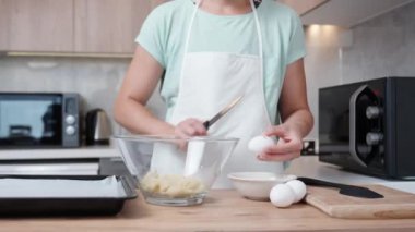 Kadın bir yumurtayı kırıyor ve onu bir tabağa döküyor. Parlak bir mutfağın arka planına karşı ahşap bir masa üzerinde..