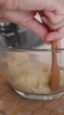 Pasta şefi choux hamur işini büyük cam bir kaseyle karıştırıyor, yakın çekim manzaralı. Dikey video.