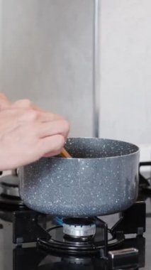 Mutfaktaki kadın tencerede bir şey karıştırıyor, gaz sobasında, ağır çekimde. Dikey video.