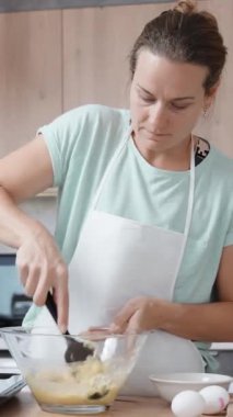 Parlak bir mutfak içinde, genç bir kadın ağır çekimde bir spatulayla choux hamur işini karıştırıyor. Dikey video.