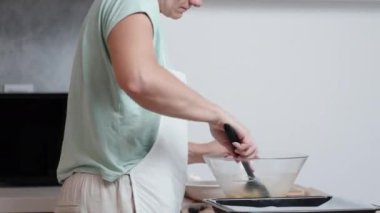 Beyaz önlüklü bir kadın choux pastası hazırlıyor. Yumurtayı bir kaseye kırıyor, yandan görülüyor..