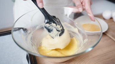 Kadın yumurtayla hamuru ağır çekimde siyah bir spatulayla karıştırıyor..