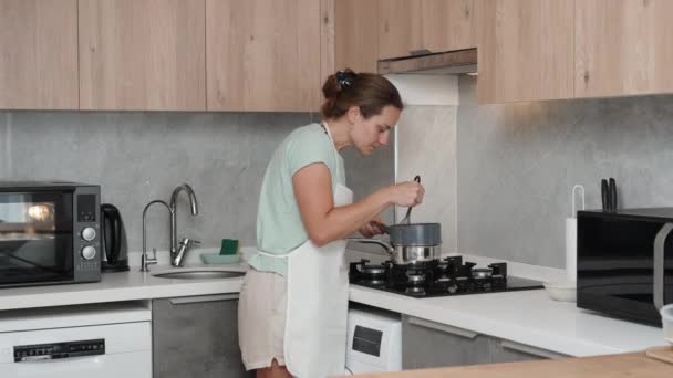 Женщина Белом Фартуке Стоит Газовой Плиты Перемешивая Кастрюле Венчиком Кухня — стоковое видео