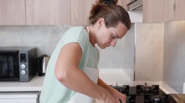 Beyaz önlüklü genç kadın, parlak bir mutfak içinde, tencerede bir şeyler karıştırıyor..