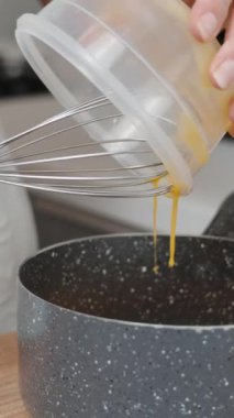 Aşçı yumurta sarısını yavaşça tencereye döküyor. Dikey video.