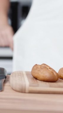 Ahşap masanın üzerinde, arka planda bir pastacı beyaz önlük giyerken ekinler var. Onların yanında çilek ve mango var. Dikey video.