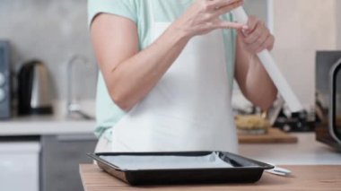 Parlak mutfak iç mimarisi. Kadın ahşap masadan kabartma kağıdını kaldırıyor ve pişirme tepsisini ortaya çıkarıyor. Yavaş çekim.