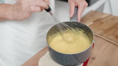 Kadın tencerede kremayı karıştırmak için çırpıcı kullanıyor. Kamera yavaş çekimde aksiyona odaklanıyor..