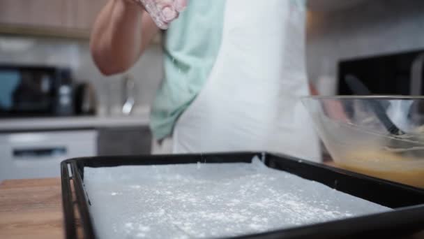 在厨房内部的背景下 一个穿着白色围裙的女人慢吞吞地从手中把面粉撒到烤盘上 — 图库视频影像